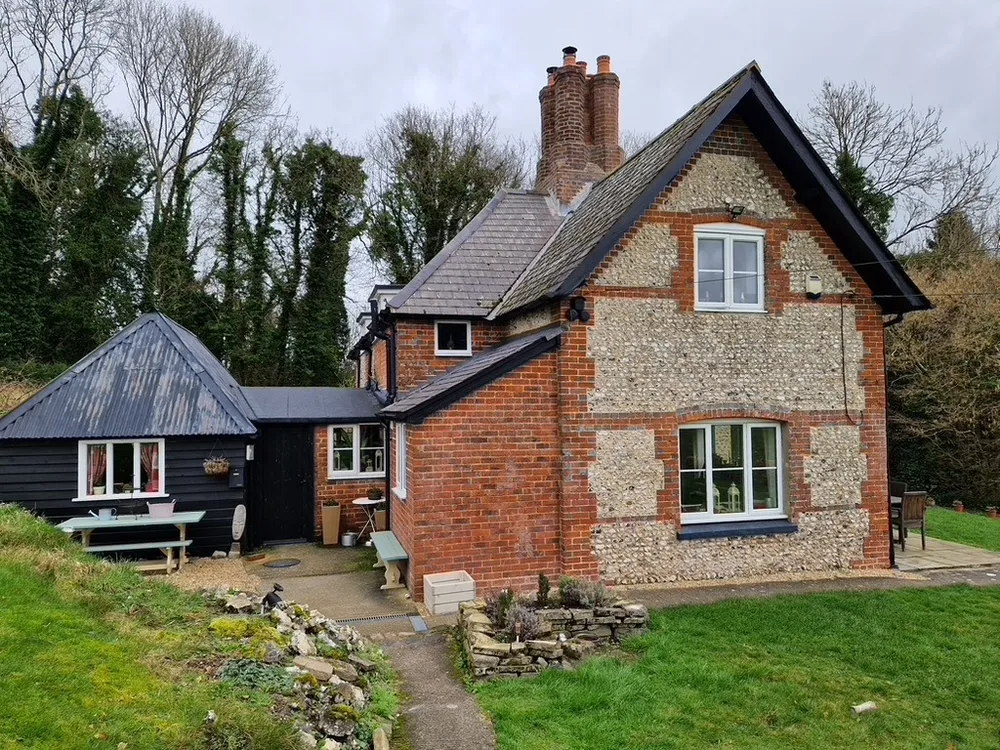 The lodge before the work: brick and flint, with the weatherboarded outbuilding alongside