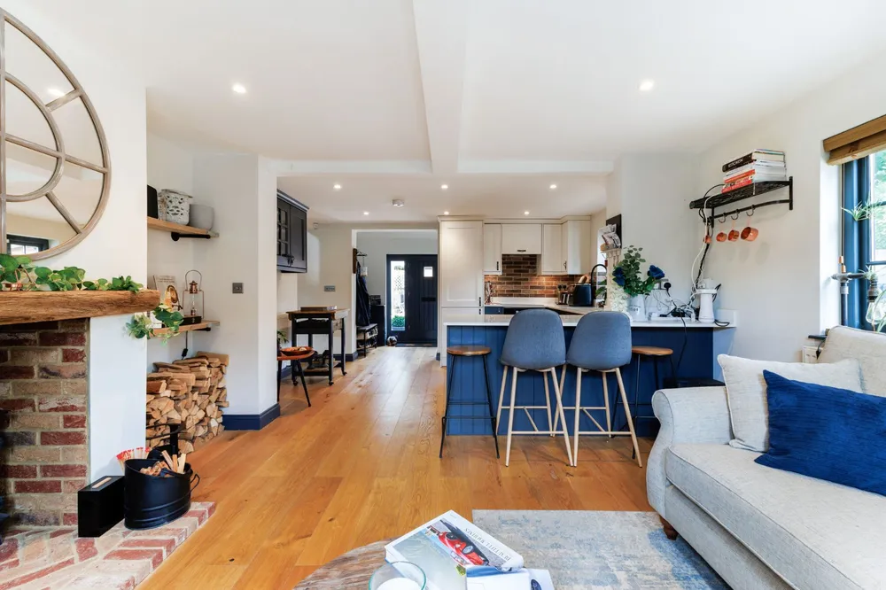 Open-plan living room and kitchen with oak floors, a brick fireplace and a blue kitchen island with bar stools