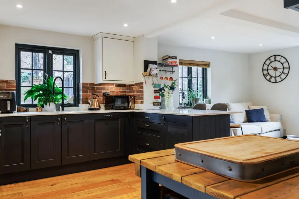 Kitchen in dark grey with white worktops, black-framed windows and a brick splashback