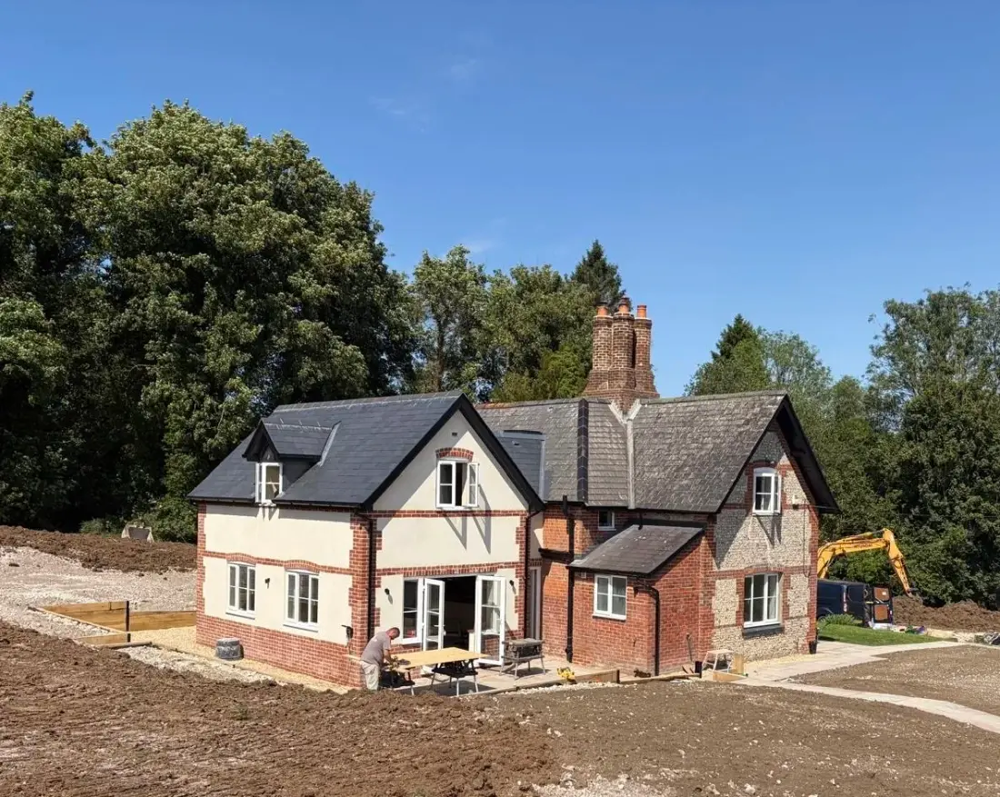 A brick and flint house with tall chimneys, its extension built and the garden being made