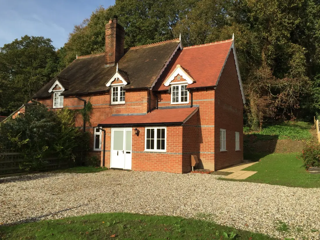 A red-brick house with a small porch and dormer windows, seen across its front garden