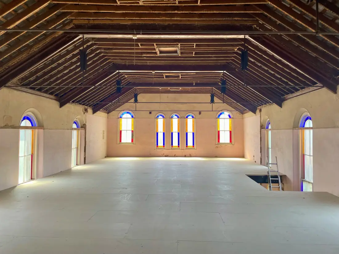 A chapel hall with arched stained-glass windows and an open timber roof