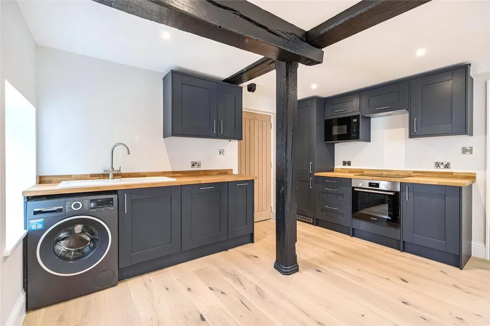 A flat’s kitchen in dark grey with oak worktops, beside an original black timber post